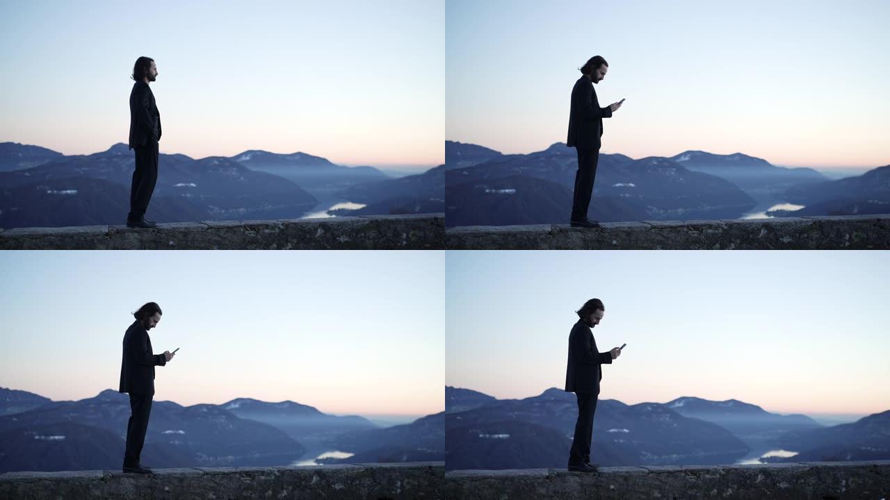 商人使用智能手机，日落光站在湖泊和山脉的视线上