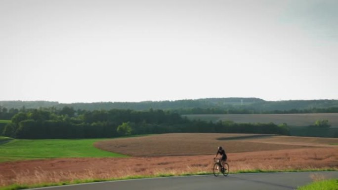 日落时在乡下骑自行车的女人。专业公路自行车手爬坡，用力推踏板。骑自行车训练。早上日出时公路骑自行车。