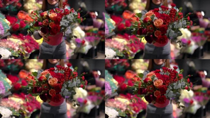 面目全非的女人用红色的花朵和绿色的树枝伸展花束，站在室内对着镜头。模糊的高加索微笑买家在花店摆姿势购
