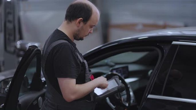 汽车修理工在修理厂使用汽车诊断工具。汽车服务经理或机械师使用带有未来派交互式诊断软件的平板电脑。