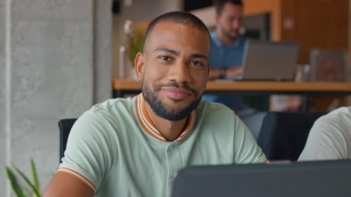SLO MO Young man在工作空间中使用笔记本电脑时对着相机微笑