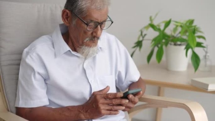 老年男子坐在扶手椅上休息时使用电话