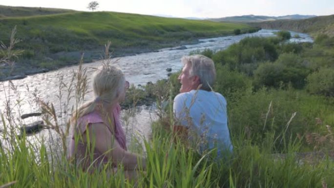 成熟的夫妇在河边的草丛中放松，远处的山脉
