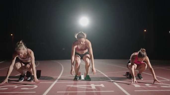 年轻漂亮的女人穿着运动服和运动鞋慢跑，一起准备在慢跑跑道上比赛。从线路出发，在黑暗中以慢动作开始比赛