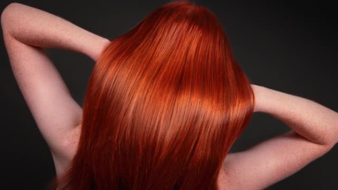 迷人的红发女人翻转她长长的直发。特写闪亮的头发波浪