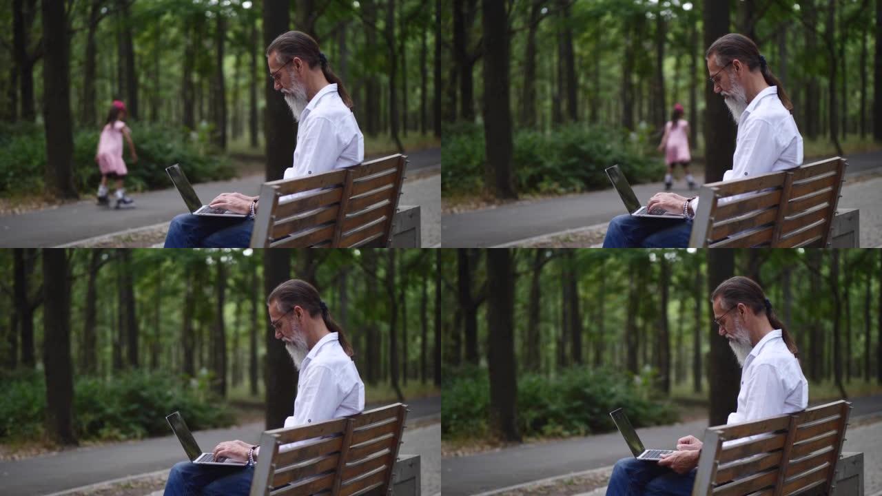 一个成年男子在公园长椅上留着灰色胡须，与笔记本电脑一起工作。一个穿着粉红色溜冰鞋的女孩在背景中经过。