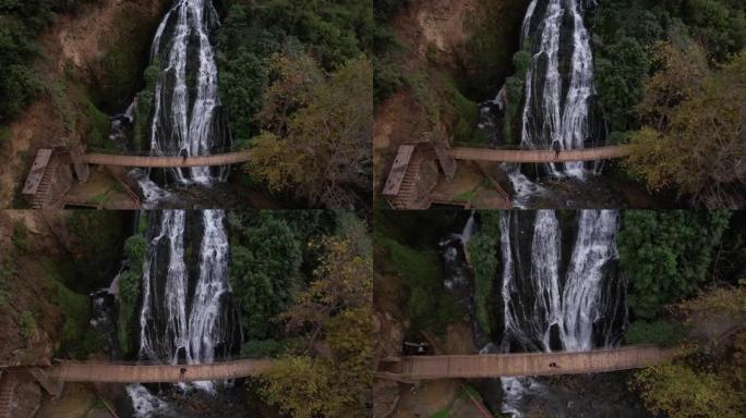 空中无人机拍摄的一名男子站在瀑布前的桥上