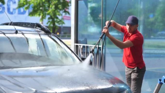 年轻的白人男性工人在阳光明媚的日子在户外用高压水洗车。英俊的男人在汽车清洁单元工作清洁车辆。工作概念