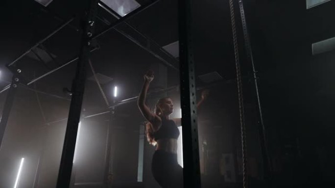 在昏暗的体育馆里，一名年轻女子在漂亮的霓虹灯背光照射下，把身子靠在单杠上。耐力和毅力拉起运动的目标