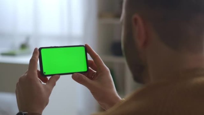 男人在手机的绿屏上观看，水平拿着，现代的小工具和用于教育，交流和娱乐的应用程序