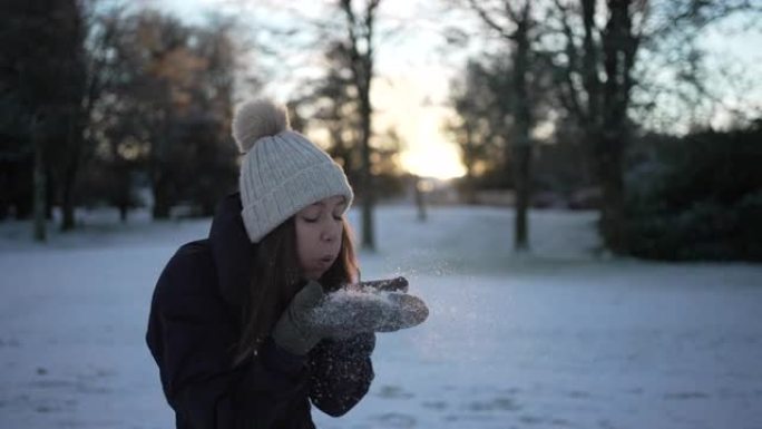 站在丘陵白雪皑皑的风景中的女人从手套上吹雪