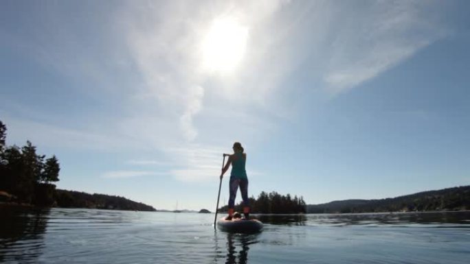 在阳光明媚的日子里，一个女人站起来在湖上划水的广角镜头