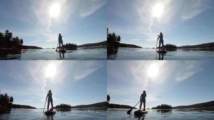 在阳光明媚的日子里，一个女人站起来在湖上划水的广角镜头