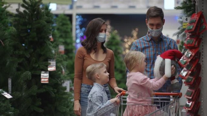 一家人选择超市里的风景。商店里戴着医用口罩的幸福家庭以慢动作购买圣诞节装饰品和礼物