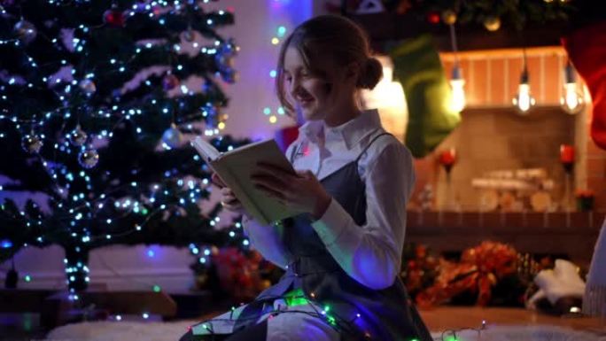 迷人的少女阅读收官书，看着微笑和梦想。放松的高加索少年在圣诞节晚上在家室内享受爱好的肖像。