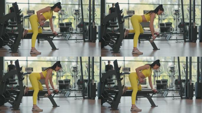 穿着运动服的西班牙裔运动员女子用哑铃训练回来，一只手靠在健身馆的长凳上