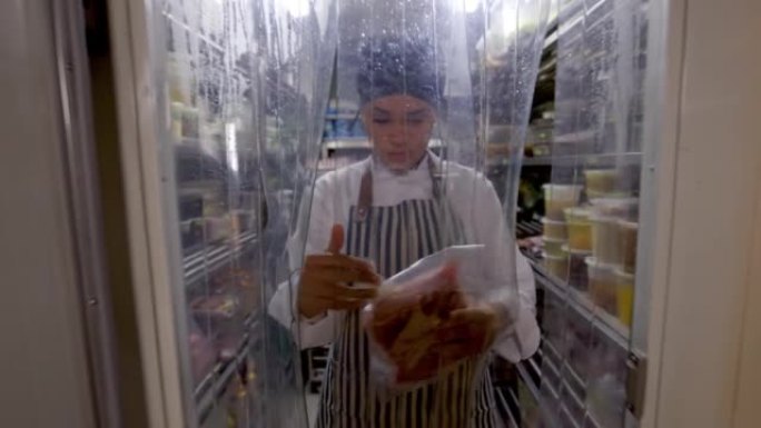 女烹饪助理从冷藏室拿出肉在餐厅准备一道菜