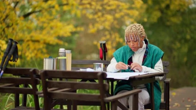 非洲民族少女看着地图和指南针，从北欧人在公园餐桌上散步休息