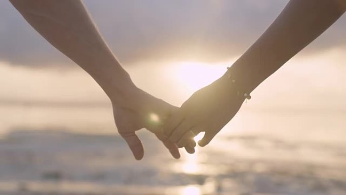手牵手的夫妇。日落海滩上紫色和橙色天空的轮廓。