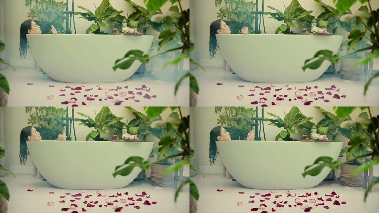 年轻女子在浴室内郁郁葱葱的绿色花园里洗泡泡浴。地板上的玫瑰花瓣