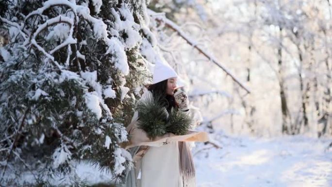 快乐的年轻女子在冬季森林散步时从保温杯中喝热茶。