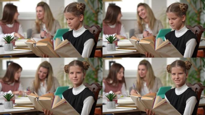 天才少女与模糊的同学和老师坐在教室里看书，看着相机微笑。聪明聪明的高加索学生在室内学校摆姿势的肖像。