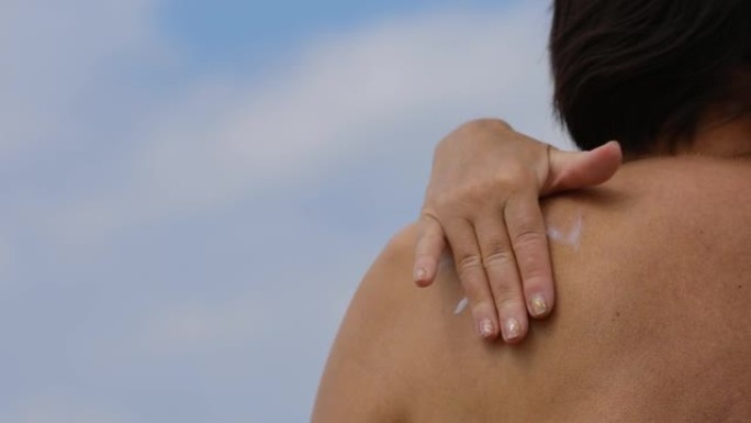 女人在晒黑的肩膀上涂抹防晒霜，以防止阳光的紫外线，在皮肤上晒日光浴之前使用防护乳液。抗衰老保护。后视