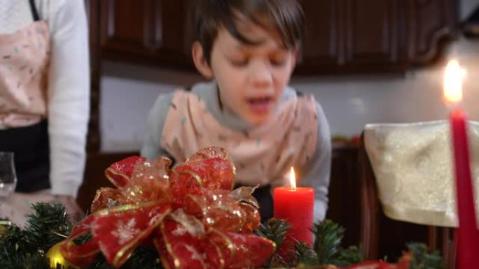 黑发男孩在厨房装饰好的新年桌子上吹蜡烛。积极可爱的高加索儿子在平安夜帮助母亲摆桌的肖像。家庭假期。