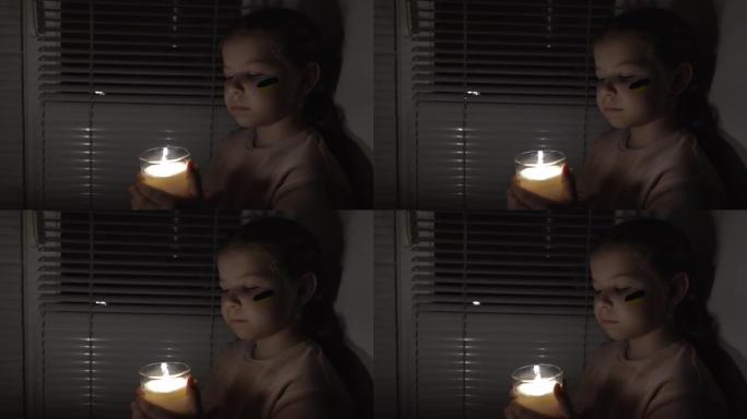 在黑暗的房间里，一个脸颊上挂着乌克兰国旗的女孩手里拿着蜡烛