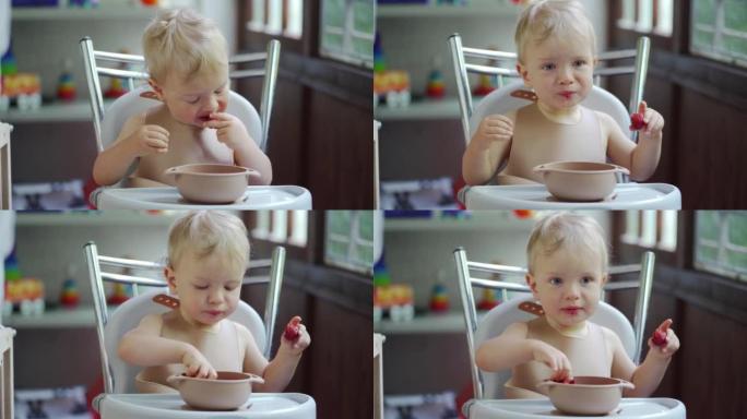 第一次吃草莓的男婴，夏天坐在高脚椅上的1.5岁蹒跚学步的孩子在阳台上吃草莓水果。