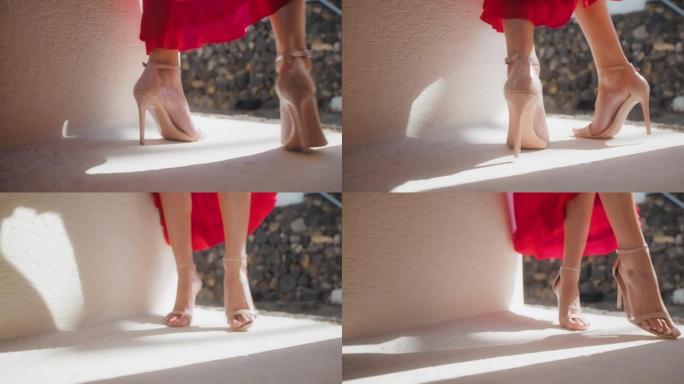 阳光灿烂的楼梯上诱人的女人。穿着红色漂亮的连衣裙。穿着高跟鞋的腿特写
