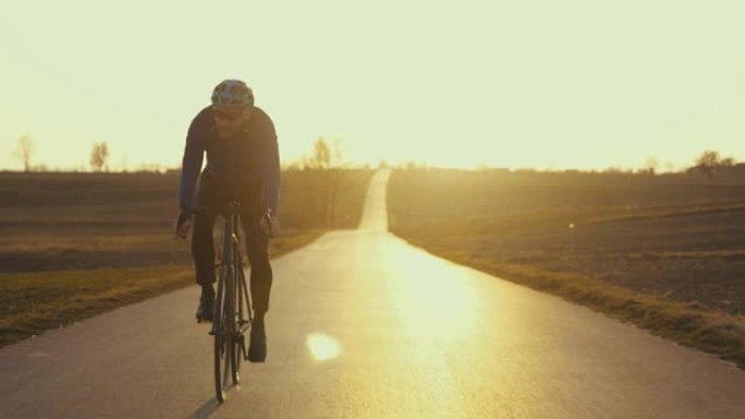 男性公路自行车手在空旷的地方超速行驶的背光轮廓。春天的日落
