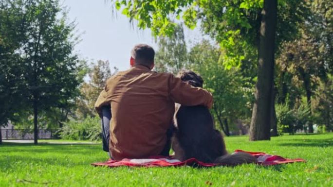 年轻人与德国牧羊犬坐在公园的草地上，这是男人最好的朋友