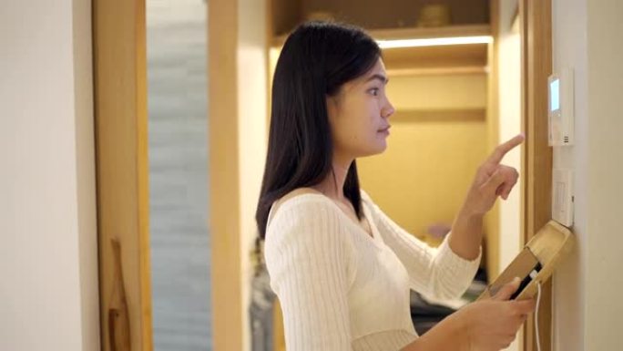 亚洲女性用家庭自动化和智能家居技术打开空调、灯和空调。