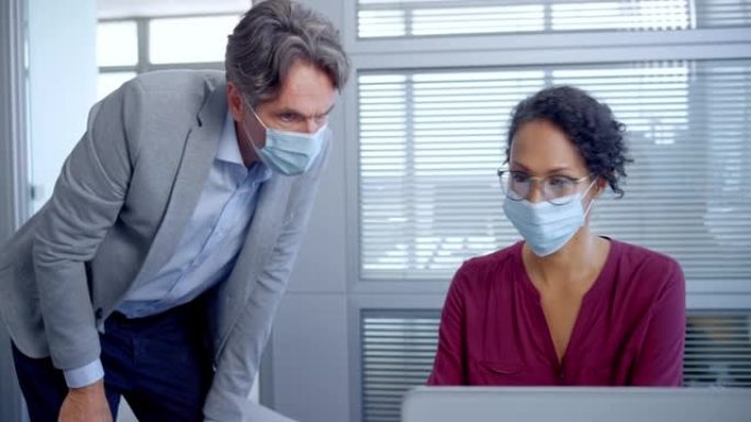 一名男子将文件带给在笔记本电脑上工作的女同事，并在戴着口罩的同时帮助她