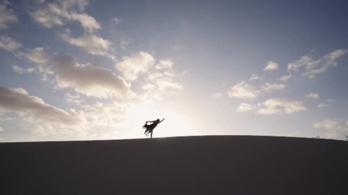 女人在沙丘上练习瑜伽，太阳在后面