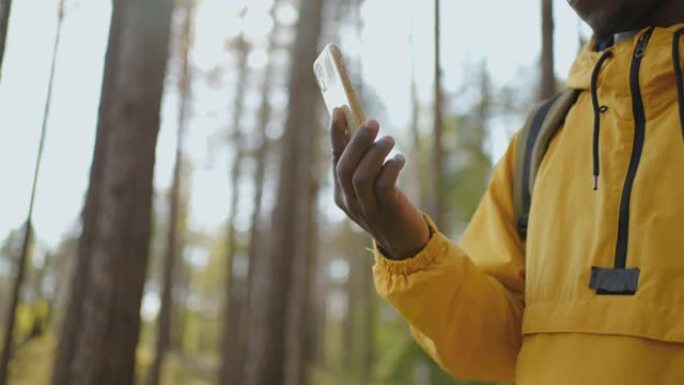 使用智能手机Gps的背包黑人。非裔美国人在森林里徒步旅行，并在智能手机上输入信息。使用智能手机的单人