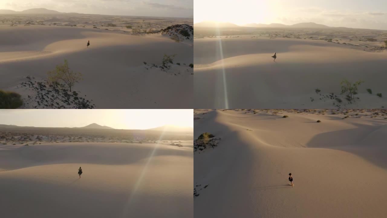 空中无人机拍摄了一名妇女在日落时独自在沙漠中行走的镜头