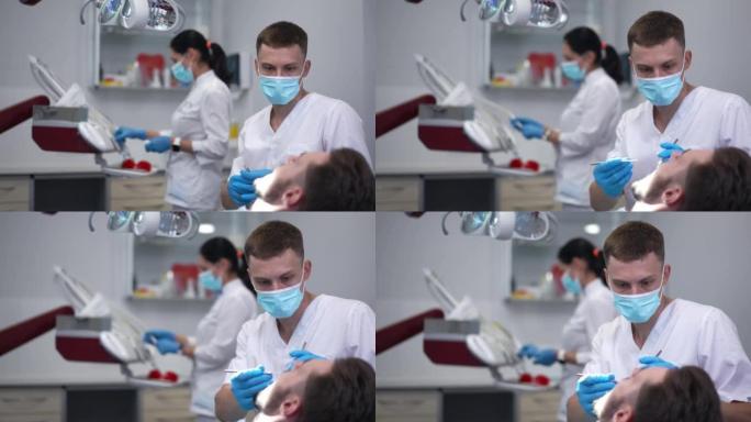 专注的专家牙医调整牙灯检查患者的口腔与工具。集中专业高加索年轻人在医院对男子进行体检的肖像。慢动作。