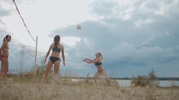 年轻的运动型女性在夏日在露天的桑迪球场上打沙滩排球，球员们在传球，进攻和盖球。