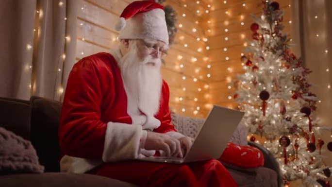 侧视图在笔记本电脑上工作的圣诞老人通过电子邮件发送圣诞节或新年的祝福或祝贺信。圣诞老人在社交网络上与