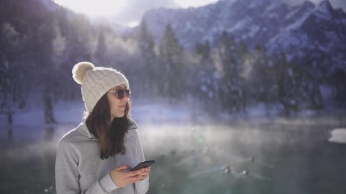 年轻女子在白雪皑皑的湖边用手机发短信