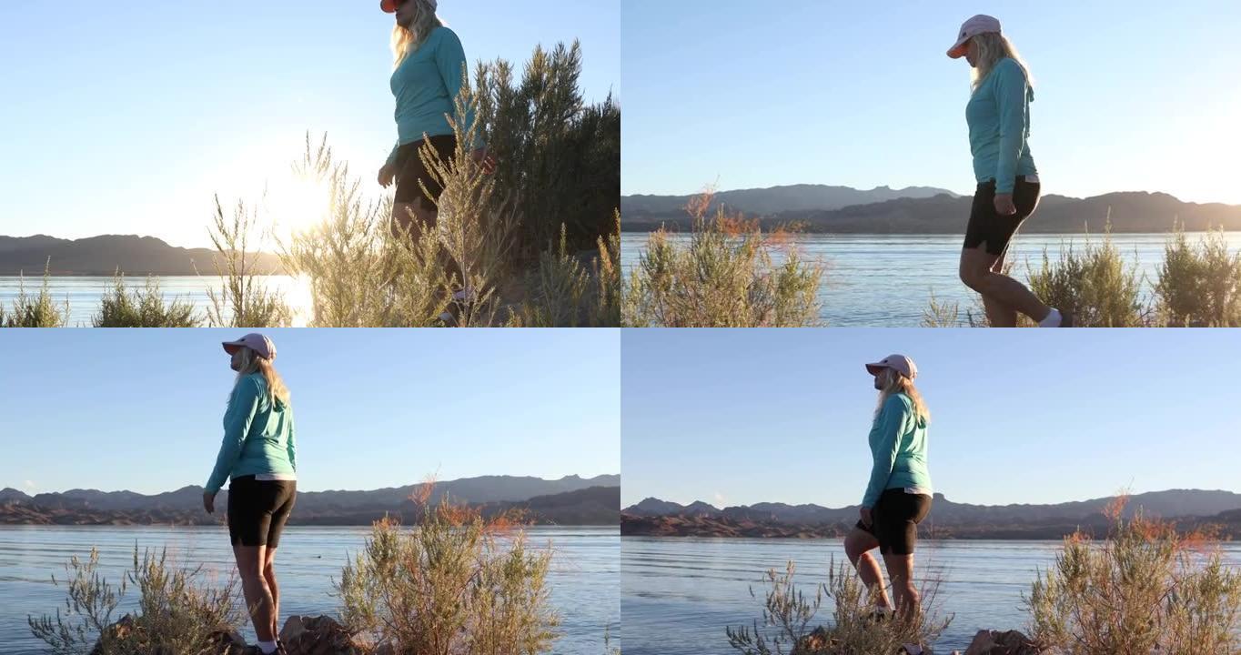 女人在日出时沿着湖岸线散步