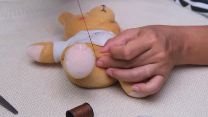 女人手工缝纫，特写。母亲用手为她的小女儿缝了一个撕破的洋娃娃。
