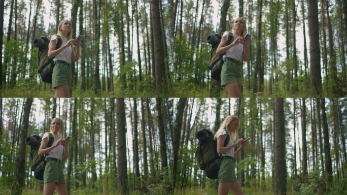 一名拿着手机的年轻女子带着慢动作的背包走过森林。使用手机中的导航器在森林中导航