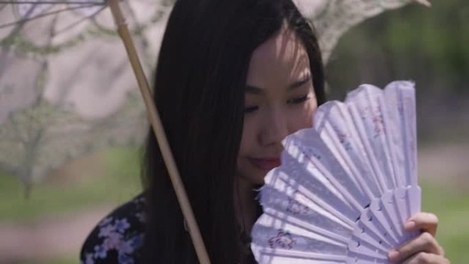 迷人害羞的亚洲年轻女子的特写镜头，白色太阳伞摇摇扇子微笑。穿着和服的美丽日本千禧一代肖像，在户外春天