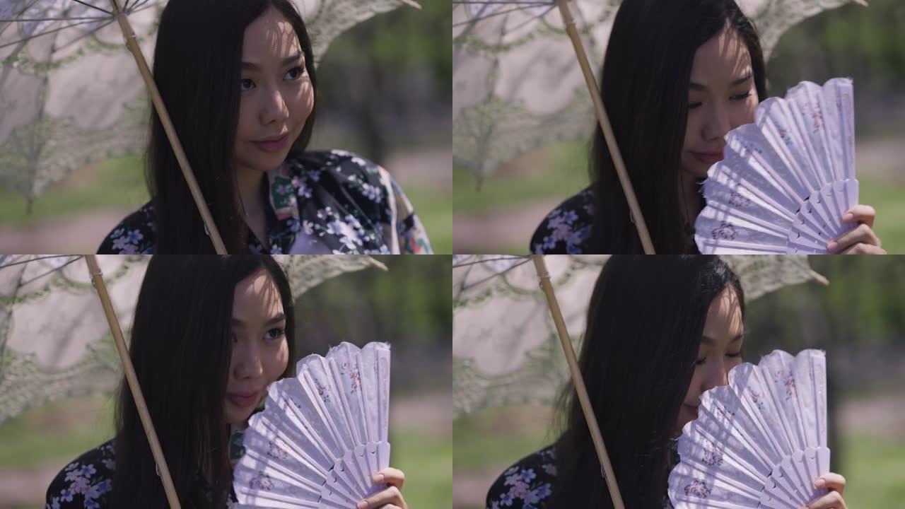 迷人害羞的亚洲年轻女子的特写镜头，白色太阳伞摇摇扇子微笑。穿着和服的美丽日本千禧一代肖像，在户外春天