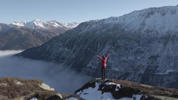 空中无人机拍摄的一名妇女在被山脉包围的山顶上摆自由姿势