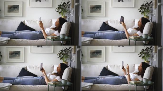 年轻女子躺在沙发上使用平板电脑