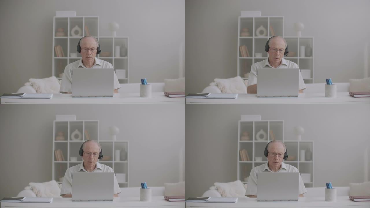 老年男老师正在网上授课，呆在家里，使用带互联网连接的笔记本电脑和耳机